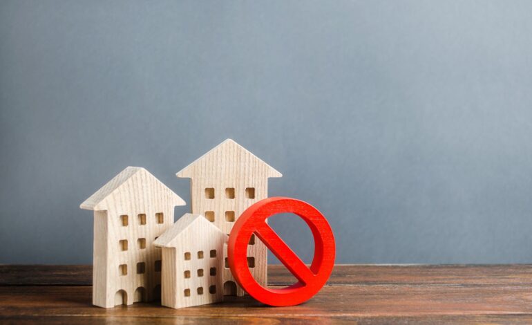 Budynki mieszkalne i czerwony symbol zakazu NIE. Niedostępne i drogie mieszkania. Brak przestrzeni życiowej i niemożność zbudowania nowej. Ograniczenia i zakazy dotyczące pięter.