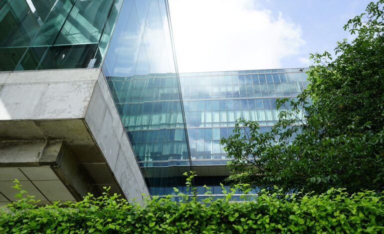 Zrównoważony zielony budynek. Ekologiczny budynek w nowoczesnym mieście. Zrównoważony szklany budynek biurowy z drzewem redukującym dwutlenek węgla. Biuro z zielonym środowiskiem. Budynek korporacyjny redukuje CO2.