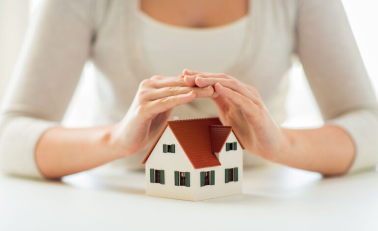 architektura, bezpieczeństwo, ochrona, nieruchomości i koncepcja nieruchomości - zbliżenie rąk chroniących model domu lub domu