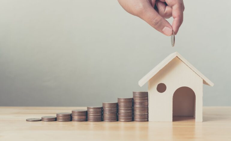 Inwestycja w nieruchomości i hipoteka na dom koncepcja finansowa Ręka wkładająca stos monet z drewnianym domem