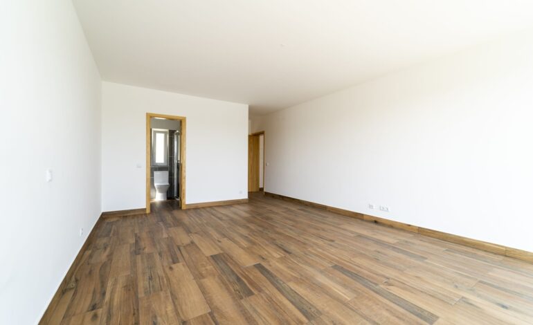 Pusty pokój z ciemną drewnianą podłogą laminowaną. Wnętrze domu, szeroka sypialnia lub pokój dzienny. Niedawno pomalowane nowe mieszkanie lub dom. Drewniana podłoga. Zarządzanie nieruchomościami