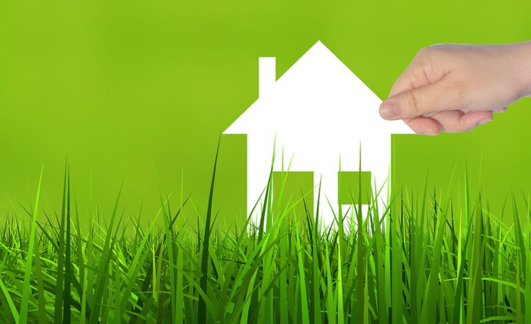 Koncepcja lub koncepcyjny symbol domu z białego papieru trzymany w dłoni przez kobietę na tle zielonej letniej trawy, metafora budownictwa, eko, ekologii, pożyczki, kredytu hipotecznego, nieruchomości, biznesu, inwestycji lub domu