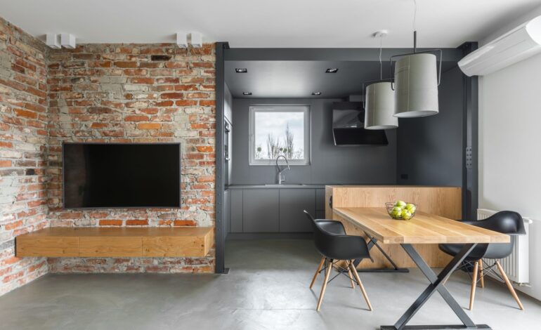 Wnętrze domu w stylu industrialnym z aneksem kuchennym, stołem telewizyjnym, krzesłami i ceglaną ścianą