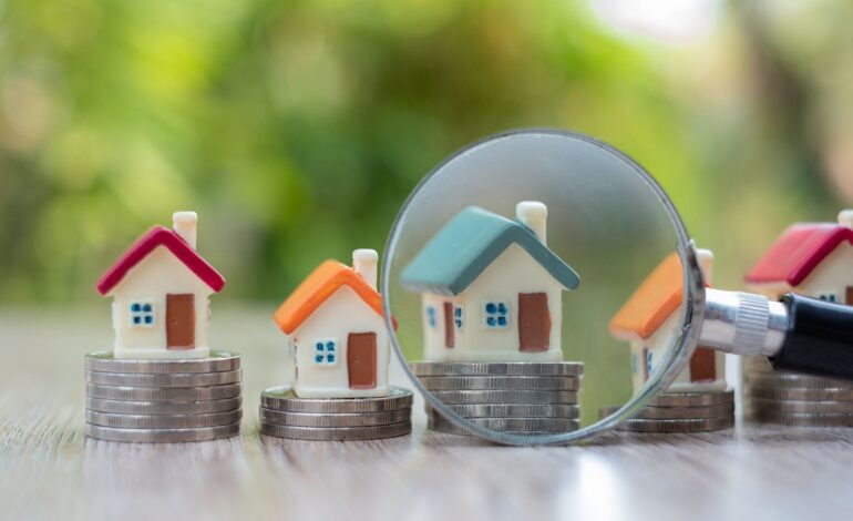 Szkło powiększające umieszczone w pobliżu modelu domu umieszczonego na stosie monet Wyszukiwanie domów, pomysły inwestycyjne, nieruchomości, kupno i sprzedaż domów, wybór domu, podatki od wynajmu, wyszukiwanie