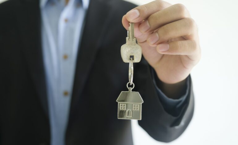 Koncepcja biznesmena z branży nieruchomości daje klucze do domu nowemu właścicielowi. Pośrednik trzyma w ręku brelok do kluczy.