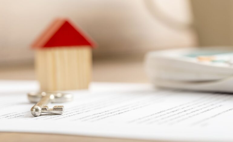 Zbliżenie umowy sprzedaży domu gotowej do podpisania z drewnianym zabawkowym kluczem do domu i kalkulatorem. Koncepcja kredytu hipotecznego i dzierżawy nieruchomości.